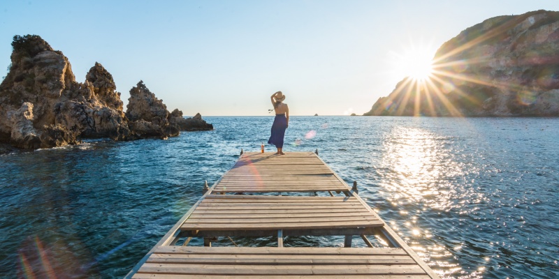 Girl watching sunset on the pier in Paleokastritsa (Corfu Island, Greece)